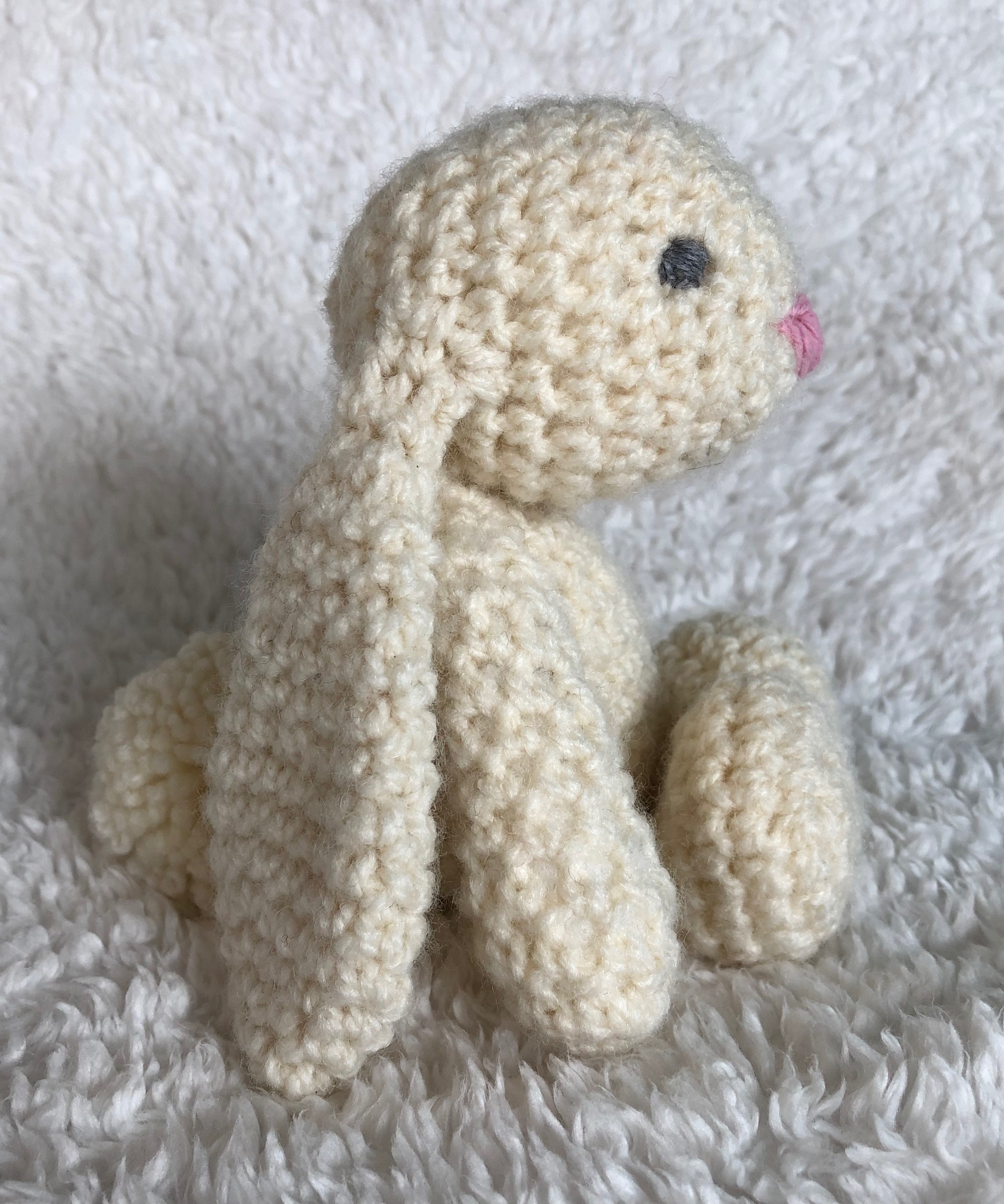 A small handmade, crocheted cream bunny rabbit with a pink crocheted heart.