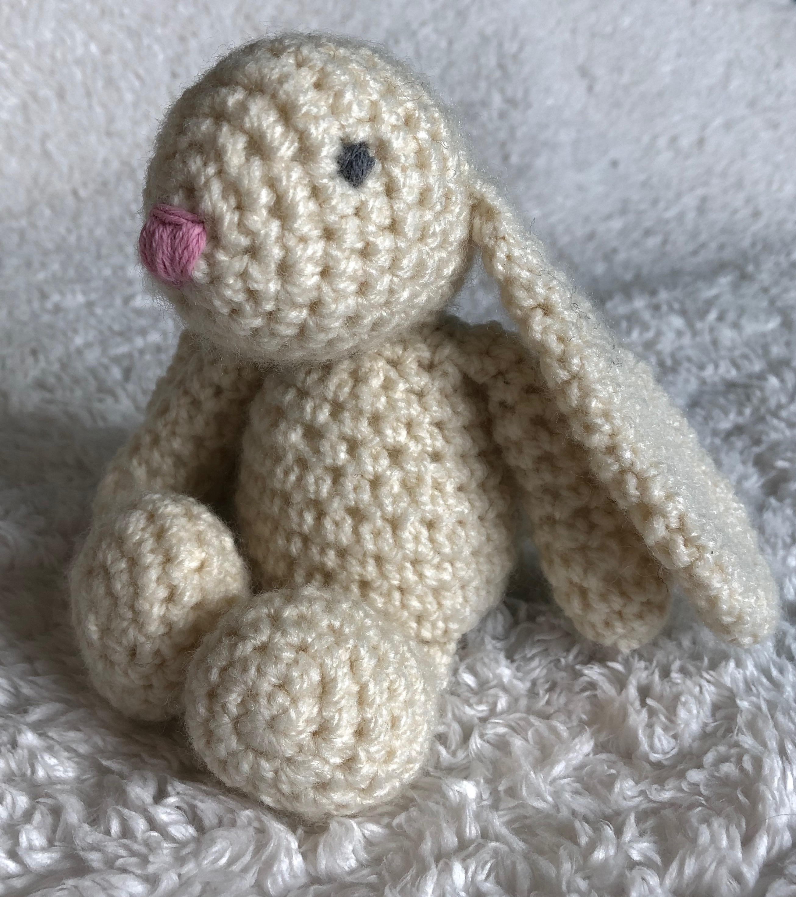 A small handmade, crocheted cream bunny rabbit with a pink crocheted heart.