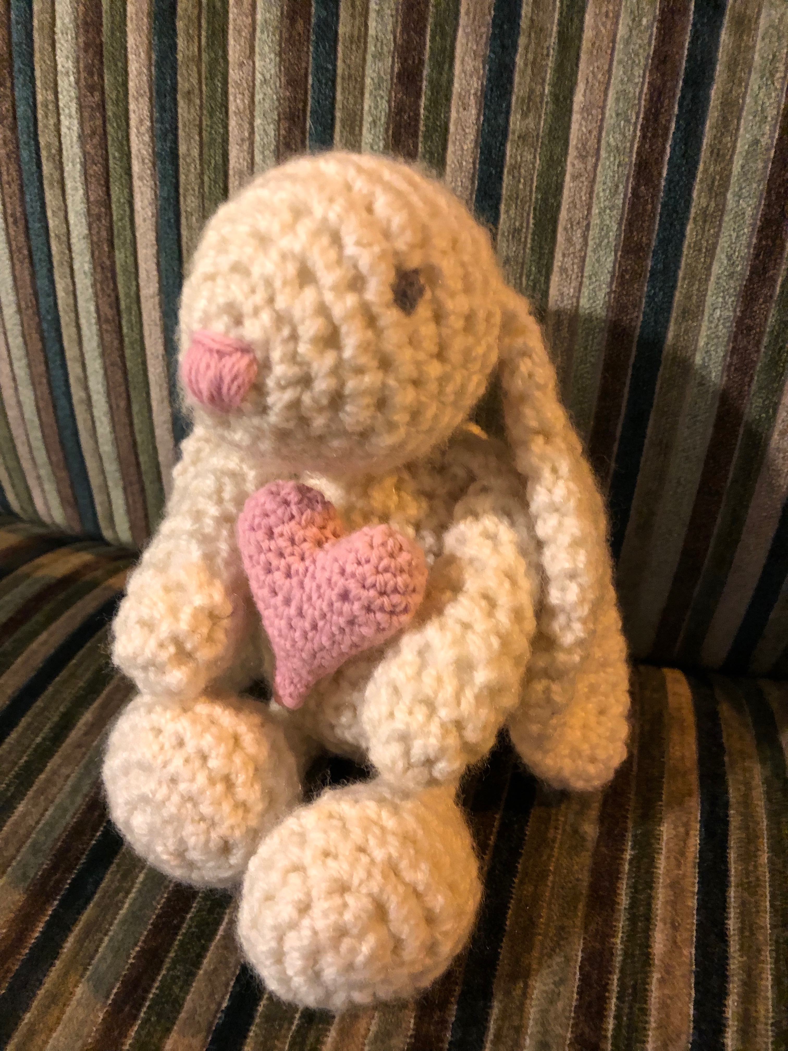 A small handmade, crocheted cream bunny rabbit with a pink crocheted heart.