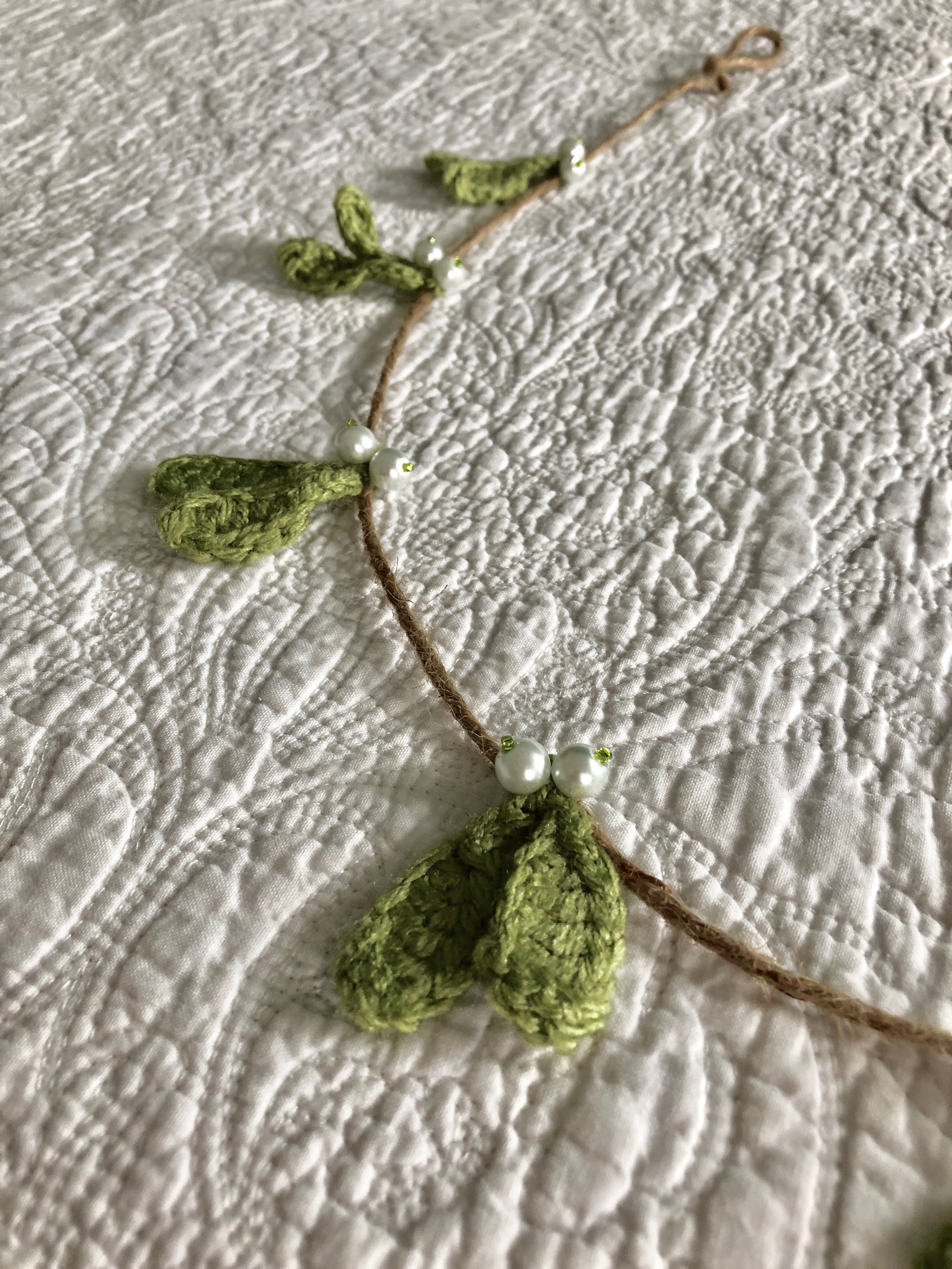 A hand crocheted mistletoe and beaded garland on jute.