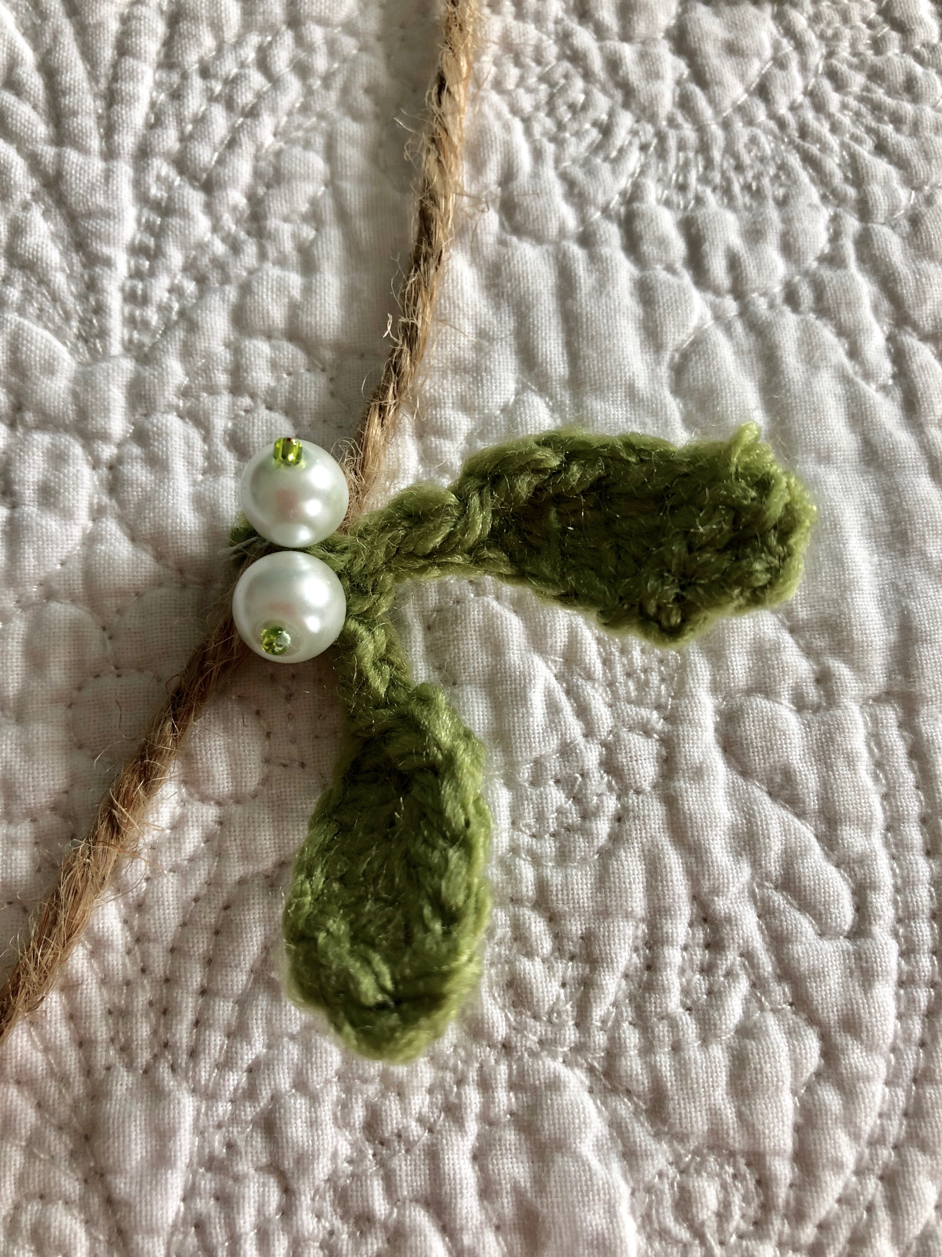 A hand crocheted mistletoe and beaded garland on jute.