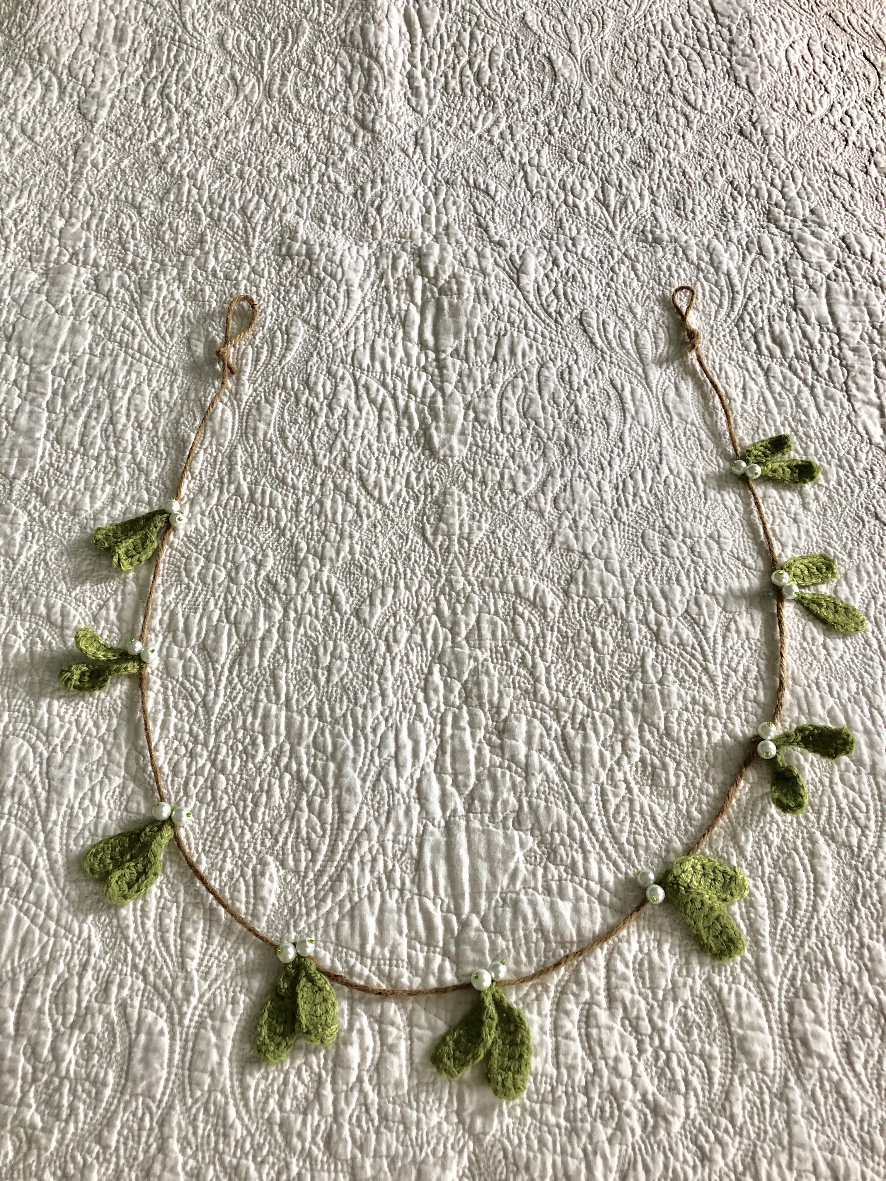 A hand crocheted mistletoe and beaded garland on jute.