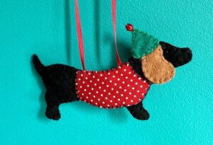 A hand made hanging decoration in the shape of a Dachshund dog. Hand cut and hand sewn in felt with a fabric coat and metal bell detail on the hat. The hanger is made of red ribbon. Approximate size 12.5cm w x 7cm h (excluding ribbon hanger) If more than one is required, please contact me directly to order. I am happy to take commissions.