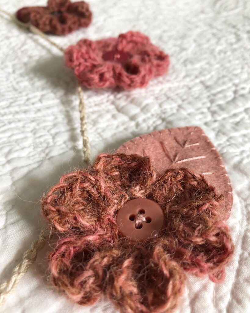 Handmade using 100% Alpaca wool and felt garland. A handmade, crocheted and sewn flower and leaf garland in a range of tonal hues. Burgundy through to Navy Blue. Seven Flower and leaf decorations along the garland.