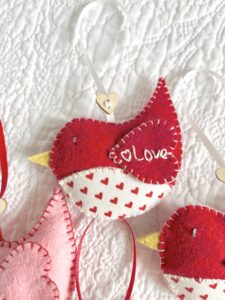 A hand cut and hand stitched, felt and fabric bird, with a cream ribbon hanging loop and wooden heart button detail. The word love is hand embroidered on the wing. Robins approximate size 8cm w x 5cm h. (excluding hanging ribbon.)