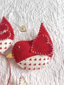 A hand cut and hand stitched, felt and fabric bird, with a cream ribbon hanging loop and wooden heart button detail. Robins approximate size 8cm w x 5cm h. (excluding hanging ribbon.) This is a decoration only, and is NOT a toy. Keep out of the reach of babies and small children due to the small parts.