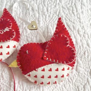 A hand cut and hand stitched, felt and fabric bird, with a cream ribbon hanging loop and wooden heart button detail. Robins approximate size 8cm w x 5cm h. (excluding hanging ribbon.) This is a decoration only, and is NOT a toy. Keep out of the reach of babies and small children due to the small parts.