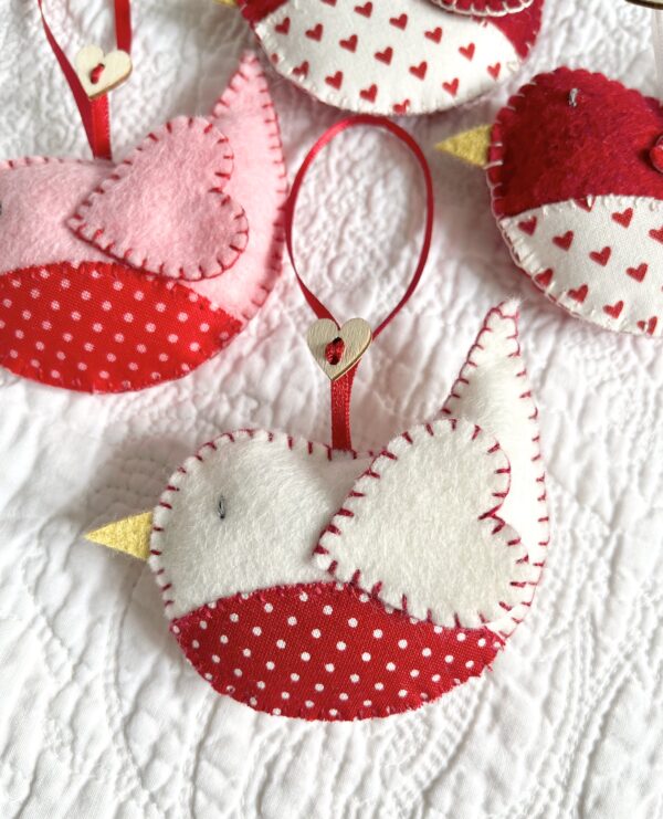 A hand cut and hand stitched, felt and fabric bird, with a red ribbon hanging loop and wooden heart button detail. Robins approximate size 8cm w x 5cm h. (excluding hanging ribbon.) This is a decoration only, and is NOT a toy. Keep out of the reach of babies and small children due to the small parts.