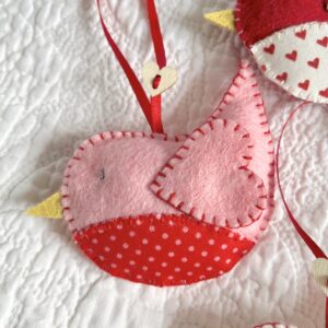 A hand cut and hand stitched, felt and fabric bird, with a red ribbon hanging loop and wooden heart button detail. This is a decoration only, and is NOT a toy. Keep out of the reach of babies and small children due to the small parts.