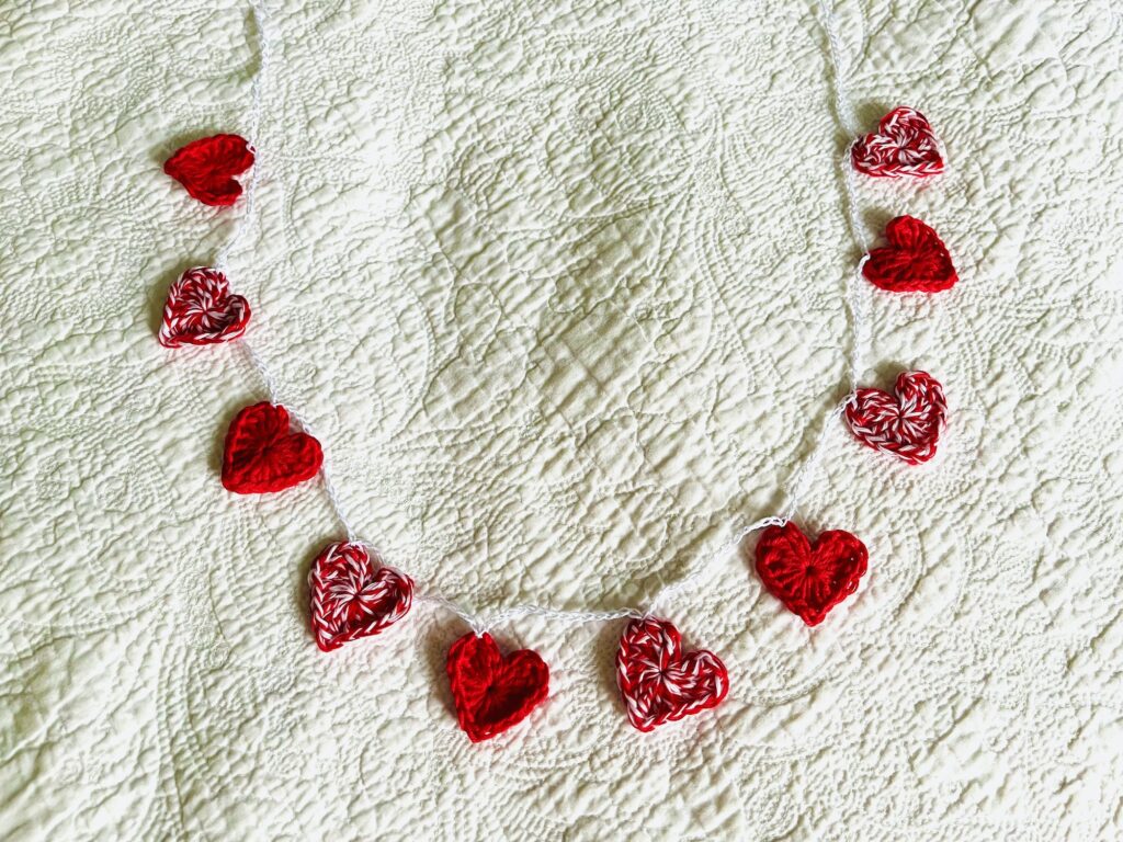 A garland of red and white and solid red crocheted cotton hearts, on a white cotton chain.