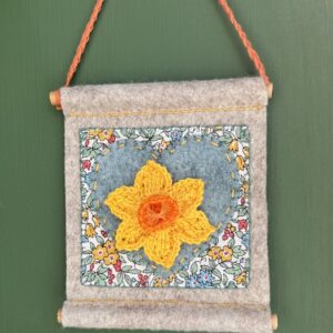 A small hand stitched decorative wall hanger, handmade using felt and 100% cotton fabric with a single crocheted Daffodil on a heart motif. The Daffodil and hanging loop are crocheted using 100% cotton. The piece is supported by 2 solid wooden dowels. The approximate measurements for this item are 9.5cm wide x 10.5cm Height x 0.8cm depth. (Not including the hanging cord.) This item is unique and handmade. No two pieces will be exactly the same. It has been designed and crafted as a hanging decoration and is not a toy. Keep away from babies and young children. Keep away from naked flames.