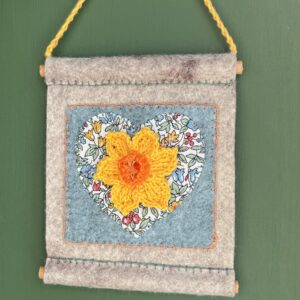 A small hand stitched decorative wall hanger, handmade using felt and 100% cotton fabric with a single crocheted Daffodil on a heart motif. The Daffodil and hanging loop are crocheted using 100% cotton. The piece is supported by 2 solid wooden dowels. The approximate measurements for this item are 10cm wide x 11.5cm Height x 0.8cm depth. (Not including the hanging cord.) This item is unique and handmade. No two pieces will be exactly the same. It has been designed and crafted as a hanging decoration and is not a toy. Keep away from babies and young children. Keep away from naked flames.