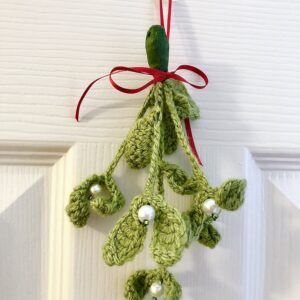 A handmade, crocheted, hanging mistletoe decoration. Made using green yarn and glass beads which are grouped and wired together and tied with a red ribbon to hang. Small size approximately 22cm high (not including ribbon hanging loop.) 5 springs of mistletoe are used in this arrangement.