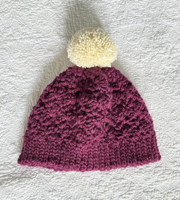 A soft and chunky textured hat with a large detachable bobble. Made in a warm cranberry colour using a very soft chunky but lightweight, 75% acrylic/ 25% Wool mix yarn. The bobble is made using a cream coloured 100% Wool. The perfect winter warmer!