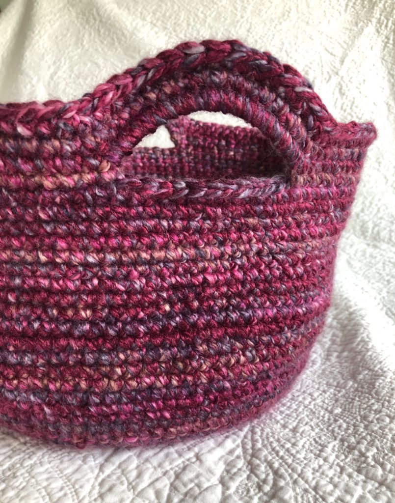 A hand crocheted multi-tonal purple basket with handles.