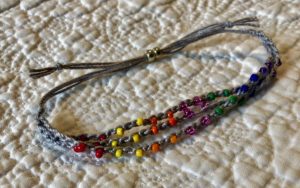 A grey cotton, crocheted and rainbow of colours glass beaded adjustable bracelet. 