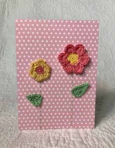 Greetings card. A pink spotty card with pink and yellow crocheted flowers and green leaves.