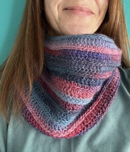 A handmade, soft textured, crocheted neck warmer, made using a soft and lightweight acrylic/wool mix yarn in shades of pinks and blues.