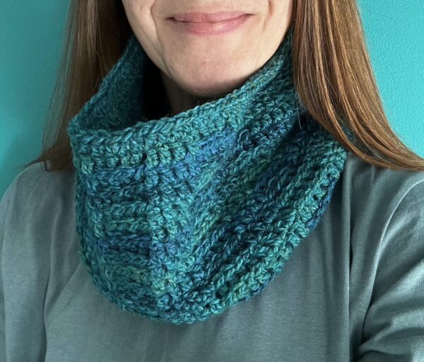 A handmade, soft textured, crocheted neck warmer, made using a soft and lightweight acrylic/wool mix yarn in shades of greens and Blues.