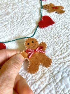 A garland of 5 mini gingerbread people and 6 red hearts. Hand-cut and handmade little gingerbread man and hearts, all made in felt, with glass beads, buttons and ribbon details, which are crocheted on to a cotton string. Approximate total length 120cm. 