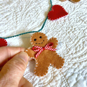 A garland of 5 mini gingerbread people and 6 red hearts. Hand-cut and handmade little gingerbread man and hearts, all made in felt, with glass beads, buttons and ribbon details, which are crocheted on to a cotton string. Approximate total length 120cm.