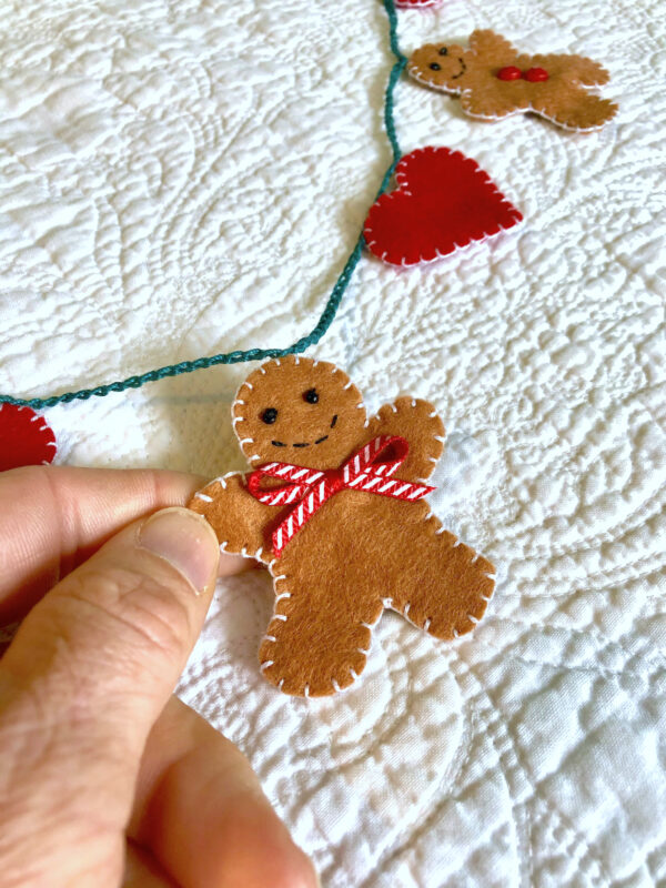 A garland of 5 mini gingerbread people and 6 red hearts. Hand-cut and handmade little gingerbread man and hearts, all made in felt, with glass beads, buttons and ribbon details, which are crocheted on to a cotton string. Approximate total length 120cm.