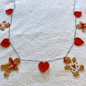 A garland of 4 gingerbread people and 5 red hearts. Hand-cut and handmade little gingerbread people and hearts, all made in felt, with fabric, glass beads, buttons and ribbon details, which are crocheted on to a cotton string. Approximate total length 125cm.