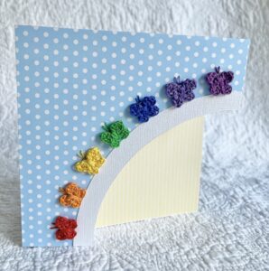 A hand cut, blue spotty card with 7 individually crocheted and hand sewn butterflies in the colours of the rainbow, arranged in an arch over a spotty yellow sun. 

This card has a blank white paper insert for you to write your own message. Envelope included.

Approximate size 15cm x 15cm. 

Handmade, using 100% cotton.