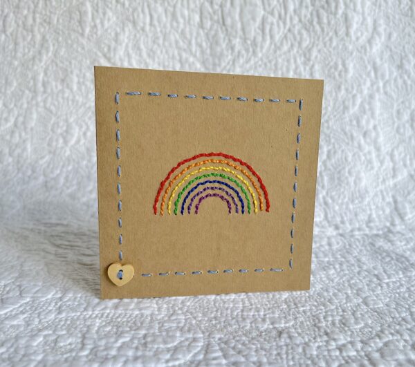 A hand stitched rainbow greetings card with wooden heart button detail. A blank, white paper insert is included for you to write your own message. Envelope included. Approximate size 10cmX 10cm. Made using 100% Cotton. Eco-friendly, Vegan friendly and fully recyclable.