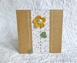 A single crocheted flower and leaf, with a hand stitched border and button detail.

This small brown card has a blank white insert for your own message, and an envelope is included.

Approximate size 10cm x 10 cm.

Made using 100% cotton.
Eco-friendly, Vegan friendly and fully recyclable.