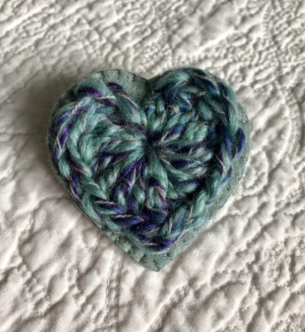 A crocheted heart on a hand stitched felt back with metal fixing brooch. Approximate size 6cm width x 6cm height.