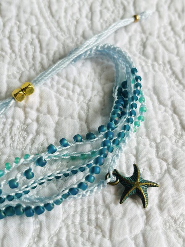 A 5 stranded, handmade and crocheted bracelet. Fully adjustable and made using glass and metal beads with antique brass coloured metal starfish charm. Made from 100% Cotton, glass and metal beads and a metal charm. No plastic! Eco-friendly, vegan friendly and completely recyclable.