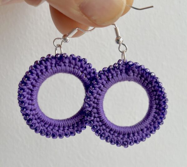 A handmade, crocheted pair of beaded hoop earrings, made using 100% cotton, glass beads and metal fixings. The earring hooks are made from a silver plated brass and are nickel, lead and cadmium free. Each earring measures approximately 3.4cm wide by 5cm Height (including hook). No plastic has been used. This item is Vegan and Eco-friendly, reusable and fully recyclable.