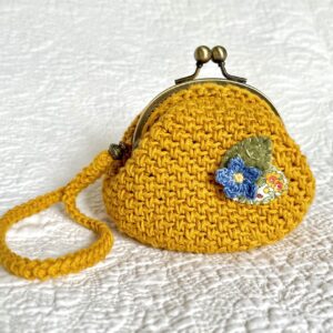 A small handmade and crocheted handheld purse. Made using 100% cotton yarn and embellished with a cotton and felt flower and leaf detail. Fitted with a solid, bronze coloured metal clasp closure, and a removable, crocheted wrist strap with brass coloured beads and clip.