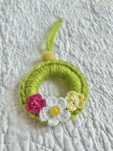 A mini crocheted and embellished Spring/Easter inspired flower wreath. Handmade using a wooden ring with a mix of acrylic, cotton and wool materials, glass beads and recycled buttons.