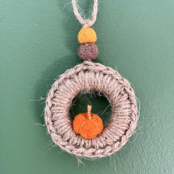 A handmade mini wreath hanging decoration. Crocheted in Jute and embellished with a mini felt pumpkin and felt balls. Handmade using a wooden ring with 100% natural Jute, and felt embellishments. Approximate size of wreath 9cm height x 6.5cm width. Not including hanging loop.