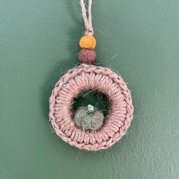 A handmade mini wreath hanging decoration. Crocheted in Jute and embellished with a mini felt pumpkin and felt balls. Handmade using a wooden ring with 100% natural Jute, and felt embellishments. Approximate size of wreath 9cm height x 6.5cm width. Not including hanging loop.