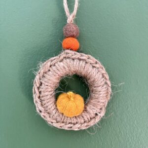 A handmade mini wreath hanging decoration. Crocheted in Jute and embellished with a mini felt pumpkin and felt balls. Handmade using a wooden ring with 100% natural Jute, and felt embellishments. Approximate size of wreath 9cm height x 6.5cm width. Not including hanging loop.