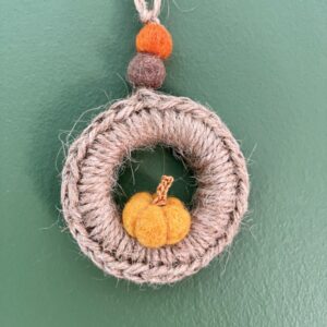 A handmade mini wreath hanging decoration. Crocheted in Jute and embellished with a mini felt pumpkin and felt balls. Handmade using a wooden ring with 100% natural Jute, and felt embellishments. Approximate size of wreath 9cm height x 6.5cm width. Not including hanging loop.