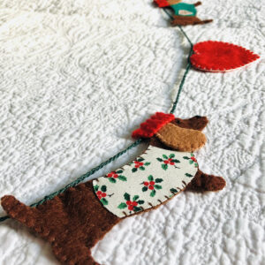 A garland of four Christmas dachshund dogs and 5 hearts. Hand cut and hand sewn, using a selection of felt and holly print cotton fabric. In a collection of red, green, brown and cream colours. Approximate total length 140cm.