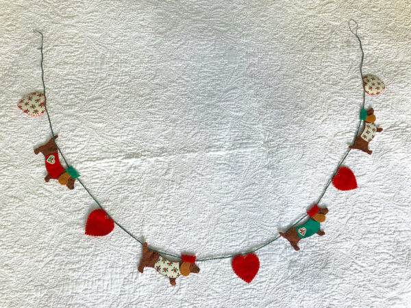 A garland of four Christmas dachshund dogs and 5 hearts. Hand cut and hand sewn, using a selection of felt and holly print cotton fabric. In a collection of red, green, brown and cream colours. Approximate total length 140cm.