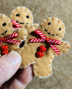 A hand-cut and handmade little gingerbread man brooch. Made in felt, with glass beads, buttons and ribbon details. The brooch has a locking metal fixing on the back. Approximate size 5cm height. 